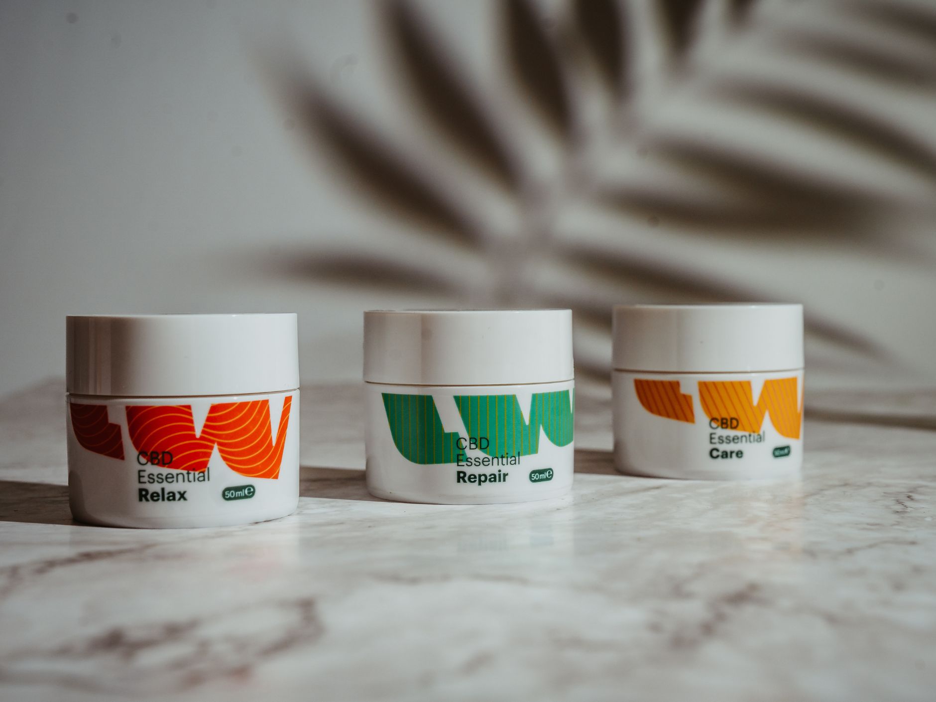 Drei Creme-Tiegel mit rotem, grünem und orangenem limewood Logo und einem Blatt das Schatten wirft