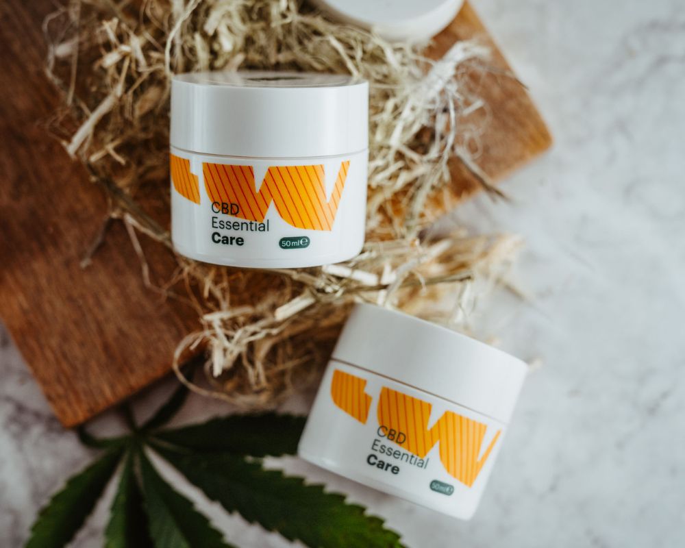 CBD Essential Care orange Creme-Tiegel auf Stroh und Holz mit Hanfblatt